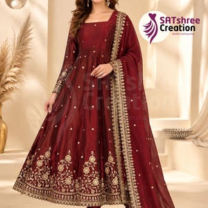 May include: A deep maroon floor-length dress with long sleeves, a square neckline, and a flared skirt. The garment features gold floral embroidery along the hem and cuffs, scattered gold sequins, and a matching sheer dupatta with a gold border.