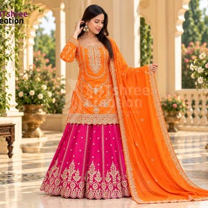 May include: A bright orange long-sleeved tunic featuring intricate gold embroidery paired with a vibrant magenta floor-length skirt adorned with gold patterns and a matching orange dupatta shawl draped over the shoulder.