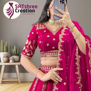 May include: A bright fuchsia Indian outfit with gold embroidery. The blouse, skirt, and sheer dupatta are adorned with detailed gold patterns. The outfit is accessorized with gold jewellery, including a necklace, earrings, and bangles. The SATshree Creation logo is visible.