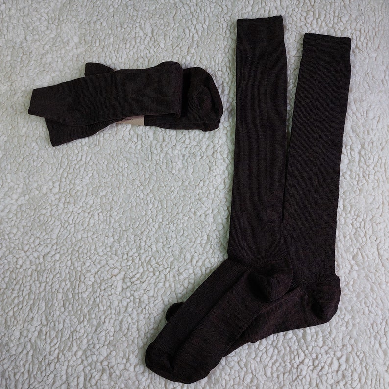 May include: A pair of brown knee-high socks. The socks are folded and laid out on a white fluffy surface.