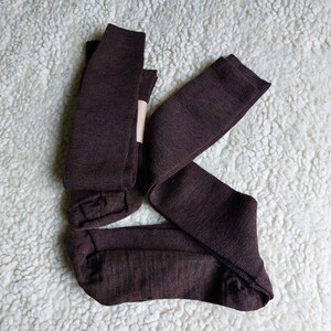 May include: Three pairs of brown knee-high socks folded together on a white fluffy surface.