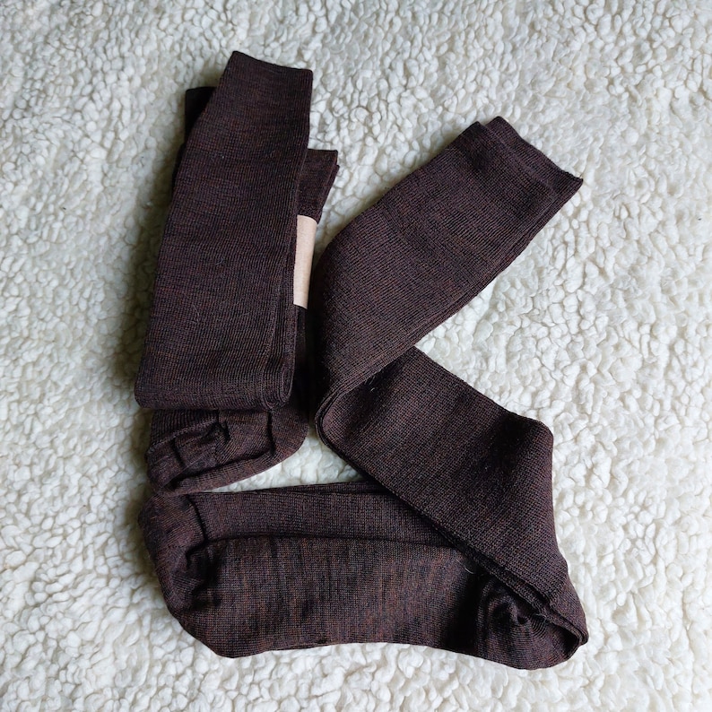 May include: Three pairs of brown knee-high socks folded together on a white fluffy surface.