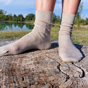 May include: A pair of beige socks with a ribbed texture, worn on a person's feet. The socks are resting on a rough, weathered tree stump.