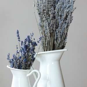 May include: Two white ceramic pitchers with dried lavender flowers. The pitchers are on a wooden surface.