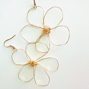 Op de afbeelding: Een paar gouden draad oorbellen in de vorm van bloemen. De oorbellen hebben een eenvoudig ontwerp met vijf bloemblaadjes en een klein midden.