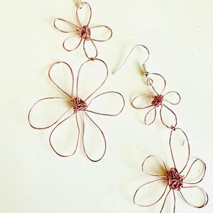May include: A pair of rose gold wire earrings with three delicate flower designs. Each flower has a center made of twisted wire.