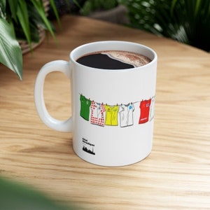 May include: White ceramic mug with a black handle. The mug has a graphic of seven colorful shirts hanging on a clothesline. The text "Dublin Marathon" is printed on the mug.