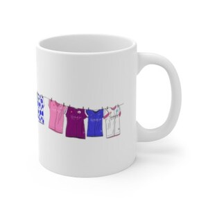 May include: White ceramic mug with a design of colorful shirts hanging on a clothesline. The shirts are pink, purple, blue, and white with polka dots.