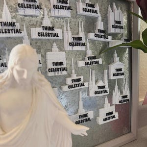 May include: A collection of white 3D-printed magnets shaped like various temple buildings, each featuring the black text "THINK CELESTIAL" attached to a metallic magnetic board, with a white statue figure positioned in the foreground.