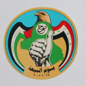 Può includere: Un adesivo rotondo con sfondo giallo e un design blu, bianco, rosso e nero. L'adesivo presenta un'immagine stilizzata di una mano che fa il pollice in su, una mappa verde del Medio Oriente e un falco con una lettera araba stilizzata in un cerchio. Il testo "يوم النبعة" e "٢٠٠٠/١/١٠" è stampato sull'adesivo.