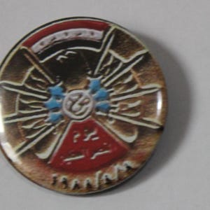 Può includere: Uno spillo rotondo dorato con un designo rosso, bianco e blu. Il centro dello spillo presenta un'aquila stilizzata con le ali spiegate, circondata da un cerchio di stelle blu e bianche. Il testo "1948/1978" è stampato nella parte inferiore dello spillo.