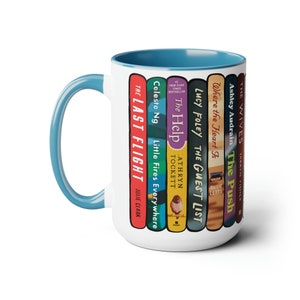May include: White ceramic mug with a blue rim and handle. The mug features a design of book spines with titles like "The Help", "The Guest List", and "Little Fires Everywhere".