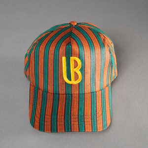 Könnte beinhalten: Eine gestreifte Baseballkappe mit orangefarbenen und grünen Streifen und einem aufgestickten gelben "UB" auf der Vorderseite.