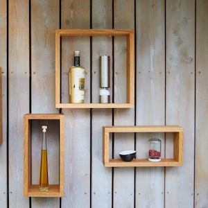 Könnte beinhalten: Vier Holzregale, die an einer Holztafelwand montiert sind. Die Regale sind leer, bis auf eine grüne Glasflasche, eine Topfpflanze, eine Flasche Öl, eine Flasche Wein, einen Pfeffermühle, eine kleine Schüssel und ein Gewürzglas.
