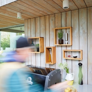 K&ouml;nnte beinhalten: Ein schwarzer Outdoor-Grill mit einer Arbeitsplatte aus Edelstahl und Holzregalen. Die Regale sind mit Kr&auml;utern, Gew&uuml;rzen und &Ouml;l gef&uuml;llt. Auf der Arbeitsplatte steht eine Sch&uuml;ssel mit Obst.