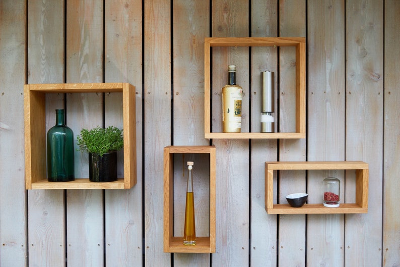 Könnte beinhalten: Vier Holzregale, die an einer Holztafelwand montiert sind. Die Regale sind leer, bis auf eine grüne Glasflasche, eine Topfpflanze, eine Flasche Öl, eine Flasche Wein, einen Pfeffermühle, eine kleine Schüssel und ein Gewürzglas.