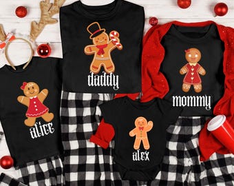 May include: A family Christmas pajama set featuring black tops with gingerbread people and names: "daddy", "mommy", "alice", and "alex". The pajamas have a black and white plaid pattern. Red accents include a cardigan and ornaments.