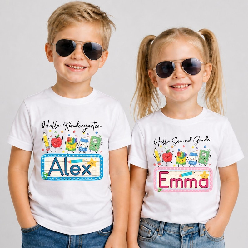 Pu&ograve; includere: Due magliette bianche a maniche corte con grafiche colorate di articoli scolastici e testo. La maglietta a sinistra riporta Hello Kindergarten e Alex, quella a destra Hello Second Grade e Emma. Entrambe presentano disegni di matita, mela, pastelli, latte e quaderno.