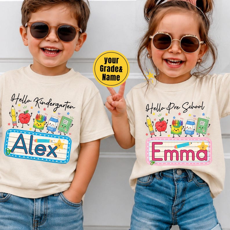 Pu&ograve; includere: Due magliette beige con grafiche colorate a tema scolastico tra cui una matita, una mela, pastelli, un cartone di latte e un quaderno. La maglietta a sinistra mostra il testo Hello Kindergarten e Alex, quella a destra Hello Pre School e Emma.