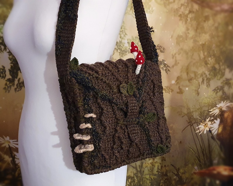 K&ouml;nnte beinhalten: Eine braune geh&auml;kelte Umh&auml;ngetasche mit Baumrindenmuster. Die Tasche hat einen Riemen und ist mit kleinen geh&auml;kelten Pilzen verziert.