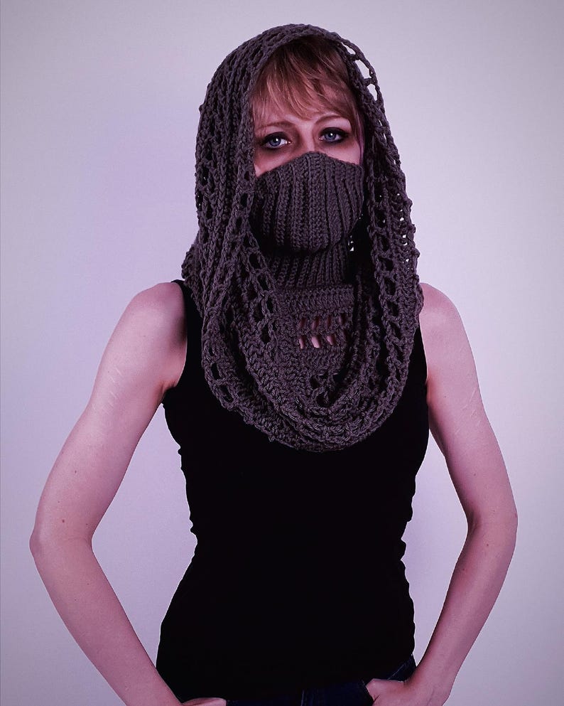 May include: A dark gray crocheted hood and cowl set. The hood features an open, lacy design around the face and head, while the cowl covers the neck and lower face. The person is wearing a black tank top.