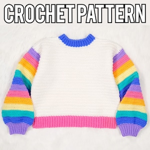 May include: A white crochet sweater with rainbow striped sleeves and a blue collar. The bottom hem is pink, and the text "CROCHET PATTERN" is at the top. This handmade sweater features a colorful, cozy design.
