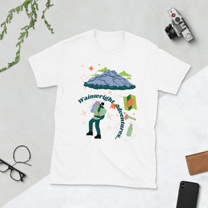 May include: White t-shirt featuring a green, blue and orange illustration of a mountain, a person hiking and the text "Wainwright adventures..."