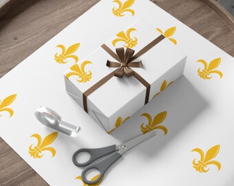Puede incluir: Papel de regalo blanco con un patrón repetitivo de flores de lis amarillas. Una caja de regalo blanca con una cinta marrón está encima del papel de regalo. Un par de tijeras plateadas y un rollo de cinta adhesiva transparente también están en el papel de regalo.