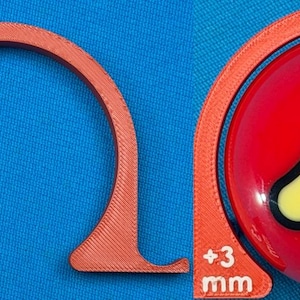 May include: An orange, semi-circular tool with "+3 mm" text, next to a red billiard ball with a yellow and black number "3" design. The tool appears to be a gauge or measuring device, possibly for pool or billiards.
