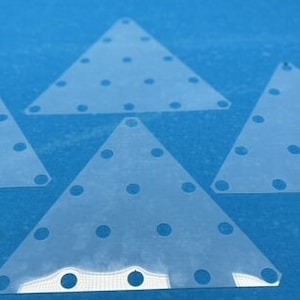 May include: Four clear plastic triangle shapes with small holes throughout. The triangles are on a blue surface.