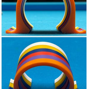 May include: A colorful, arched pool table accessory. The object is orange with layers of yellow, blue, purple, and red. The accessory is designed to hold pool balls.