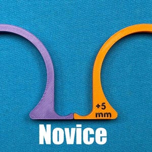 May include: Two arched, semi-circular tools, one purple and one orange, with measurements of +4 mm and +5 mm, respectively. The word "Novice" is printed in white below the tools. The tools are on a blue background.