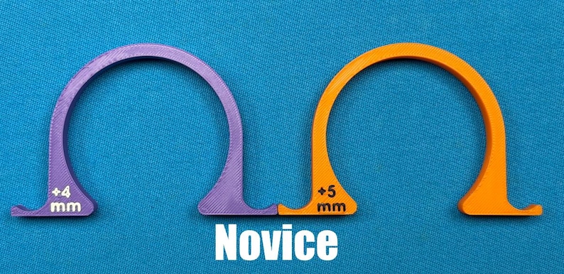 May include: Two arched, semi-circular tools, one purple and one orange, with measurements of +4 mm and +5 mm, respectively. The word "Novice" is printed in white below the tools. The tools are on a blue background.