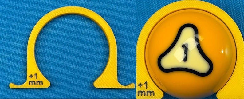 May include: A yellow 3D-printed tool with a curved design, featuring a measurement of +1 mm. The tool is positioned next to a yellow billiard ball with a black and white graphic of the number 1.