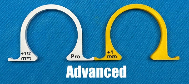 May include: Two arched, semi-circular tools, one white and one yellow, with a blue background. The white tool has the text "+1/2 mm" and "Pro". The yellow tool has the text "+1 mm". The word "Advanced" is below.