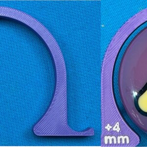 May include: A purple, semi-circular tool with a flat base and the text "+4 mm" printed in white. The tool is positioned next to a purple billiard ball with a yellow and black number four graphic.