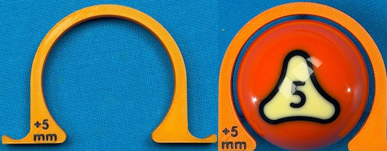 May include: An orange pool ball with the number 5 inside a white and black triangle, next to an orange curved guide. The guide has "+5 mm" printed on it. The background is blue.