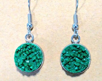 May include: A pair of dangle earrings with a silver-tone metal setting. Each earring features a round, bright green, textured stone. The earrings have a simple hook design for pierced ears.