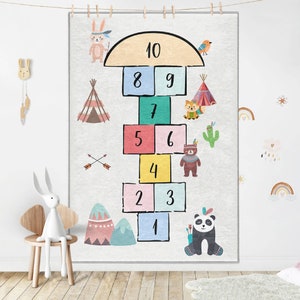 Op de afbeelding: Een kleurrijk hinkelspelkleed met een sprookjesachtig bosmotief. Het kleed heeft de nummers 1-10, een tipi, een cactus, een vos, een beer, een panda, een konijn en een vogel.