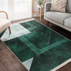 Può includere: Un tappeto rettangolare con un motivo geometrico nei toni del verde e del bianco, accentuato da linee dorate. Il tappeto ha un bordo con frange ed è posizionato su un pavimento in legno. Le dimensioni del tappeto non sono visibili.