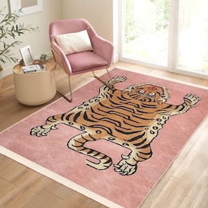 Puede incluir: Una alfombra rosa con un gran diseño de tigre naranja y negro. El tigre está tumbado de espaldas con las patas extendidas. La alfombra tiene un borde blanco.