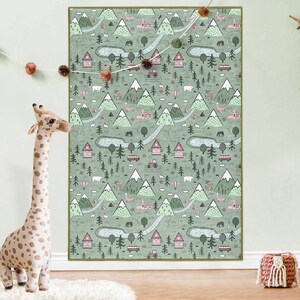 May include: A green and pink illustrated children's rug with a repeating pattern of mountains, trees, houses, and animals.