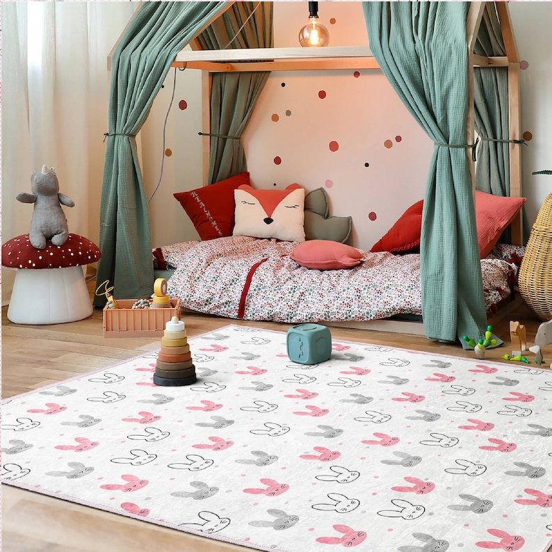 May include: A white play mat with a pink and gray bunny rabbit pattern. The mat is in a room with a wooden bed with green curtains and a fox pillow.