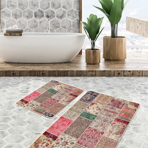 May include: Two patterned bath mats in a bathroom setting. The larger mat is a patchwork design with various colors and patterns, including red, pink, green, blue, and brown. The smaller mat is a similar design but smaller in size.