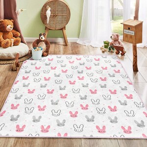 May include: A white and pink play rug with a repeating pattern of gray bunny faces. The rug has a pink border.