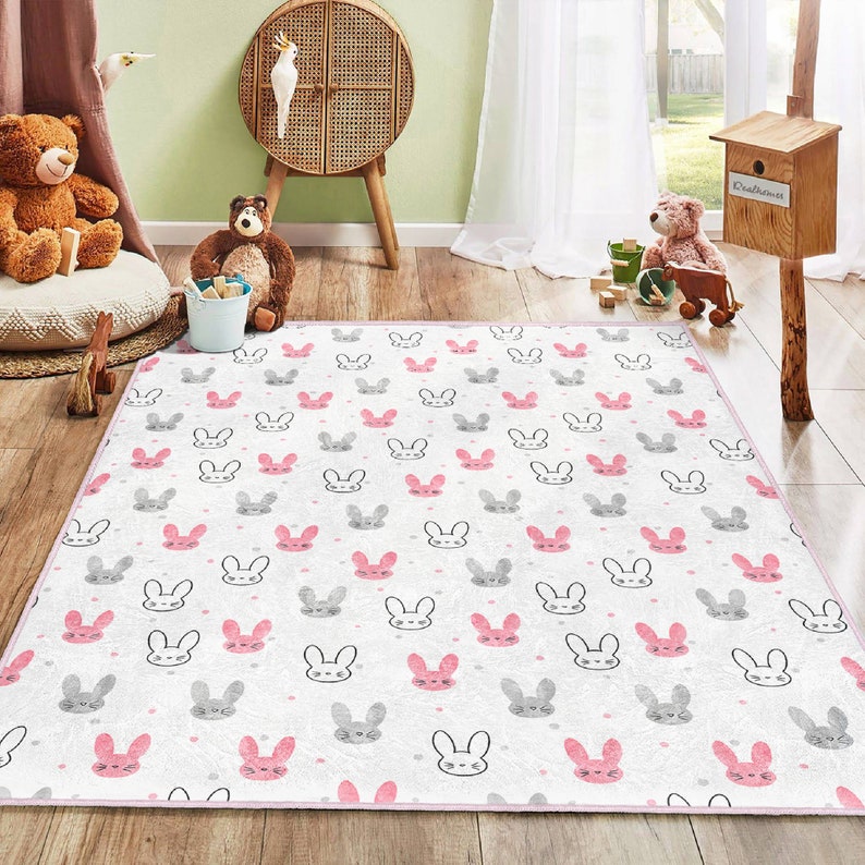 May include: A white and pink play rug with a repeating pattern of gray bunny faces. The rug has a pink border.