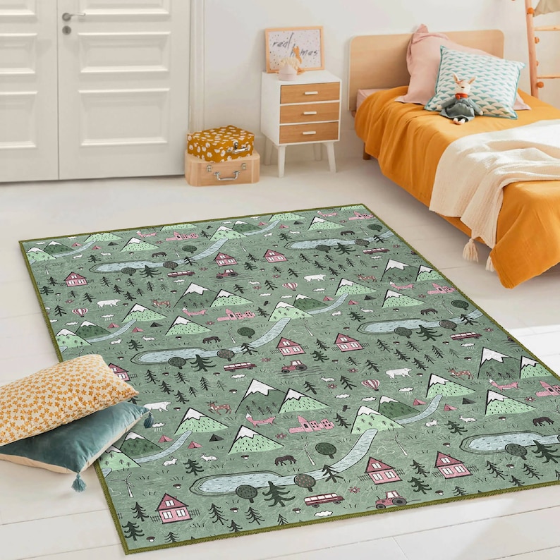 May include: A green and pink patterned rug with a whimsical design featuring houses, mountains, trees, and other nature-inspired elements. The rug has a light green background with pink accents and a green border.