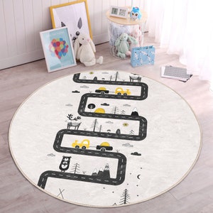 May include: A round, white play rug with a black winding road design. The road has yellow cars, trees, mountains, and a deer on it. The rug has a beige border.