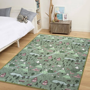 May include: A green and pink area rug with a whimsical design featuring mountains, trees, houses, and other woodland elements. The rug has a light green background with pink accents and a light green border.