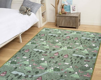 May include: A green and pink area rug with a whimsical design featuring mountains, trees, houses, and other woodland elements. The rug has a light green background with pink accents and a light green border.